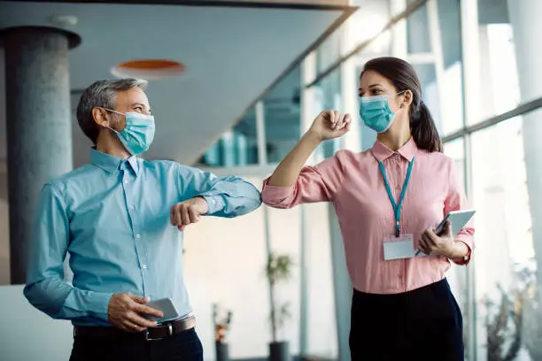Photo of Happy colleagues greeting with elbows in a hallway during coronavirus pandemic.