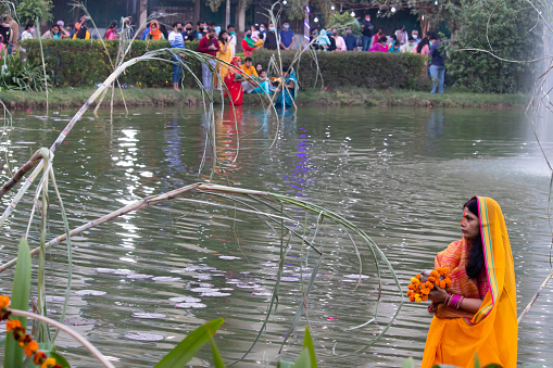 Noida Uttar Pradesh India 20 November 2020 - Married Hindu Devotee In Golden Saffron Traditional Sari Carrying Flowers In Hand And Offering Arghya Prayers To Surya Dev On Auspicious Chhath Festival