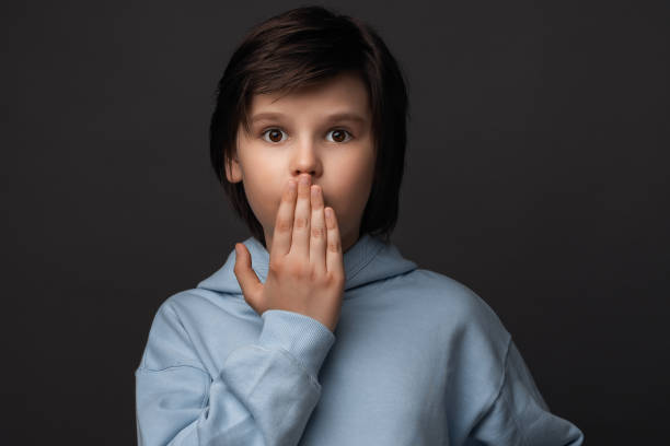 istock Cute boy 10-12 years old holds hand on lips. Silence and secret concept. Studio shot, gray background 1287549874
