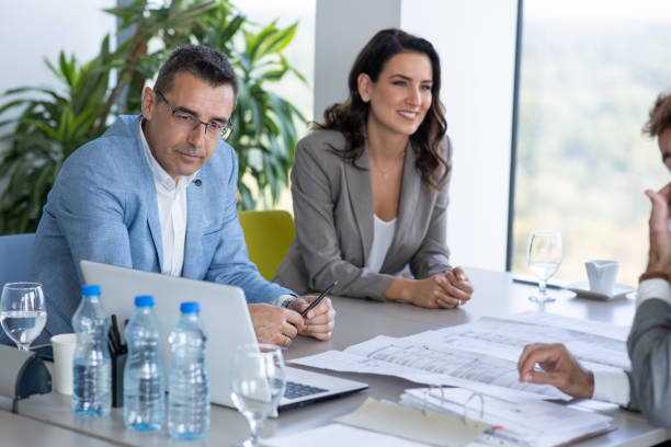 istock Businessman at the conference table looking at laptop, his colleagues analyzing spreadsheet 1287550008