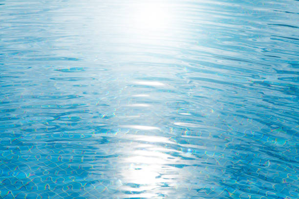 Close-up view of rippling blue water with sunlight reflections on a swimming pool surface, creating a calming abstract pattern.