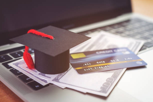 istock Credit card, Academic hat model and Notebook on wooden desk. Online payment by using laptop 1287550933
