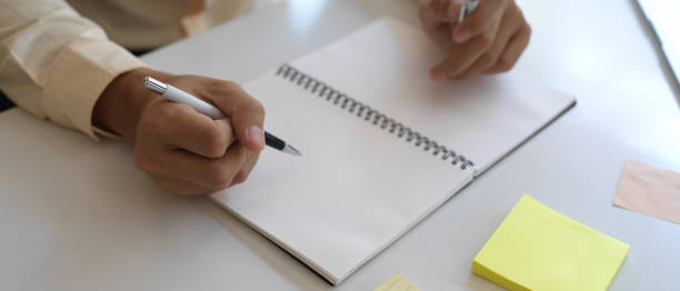 istock Male hand writing on blank note book on meeting table with stationery 1287550987