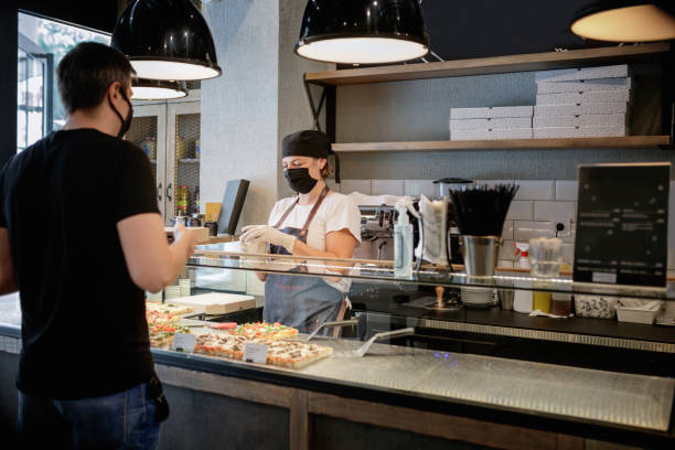 istock Woman with protective face mask and gloves closing disposable coffee cup for customer 1287551777