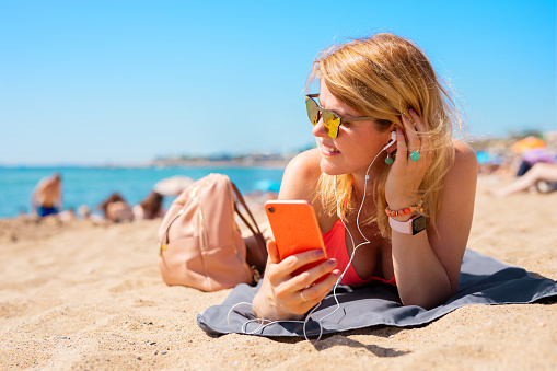 Woman listening to music while relaxing on the beach in hot summer day