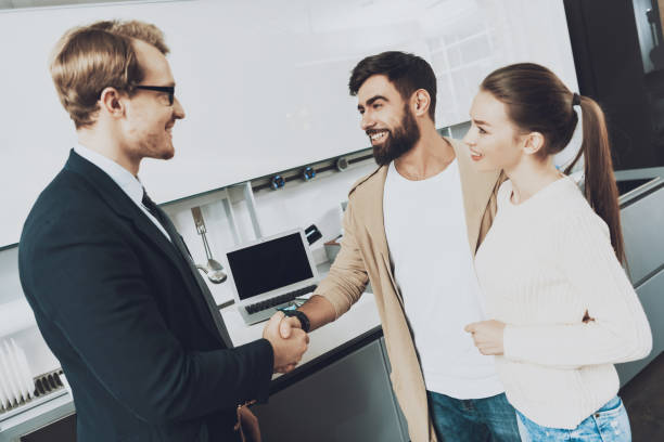 Manager and client with wife are shaking hands in kitchen store with laptop on background. stock photo