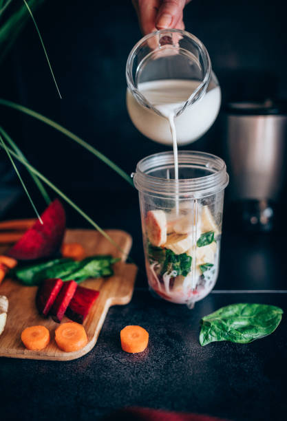 A woman's hand in the kitchen pours milk for smoothies