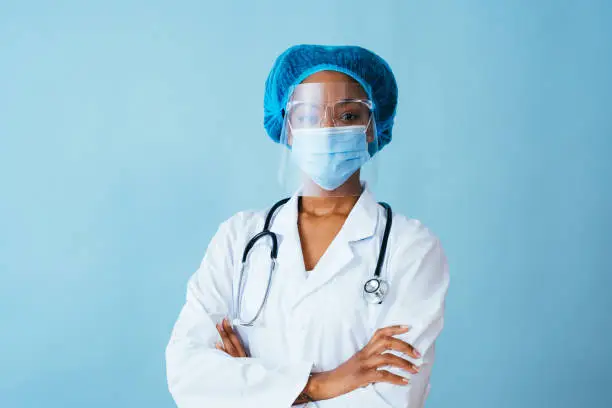 Portrait of a doctor in lab coat with face mask, face shield,  and hair ppe with arms crossed