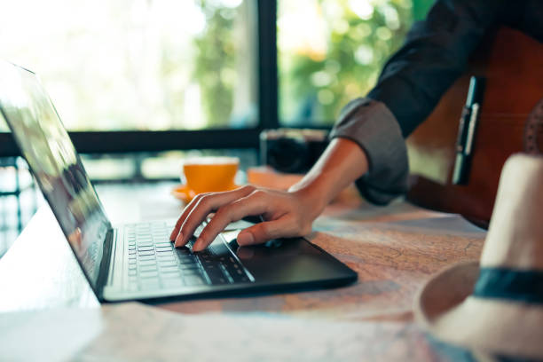 istock Man' hand use laptop for search holiday reservation. Map, book and hat on the table. 1287562144