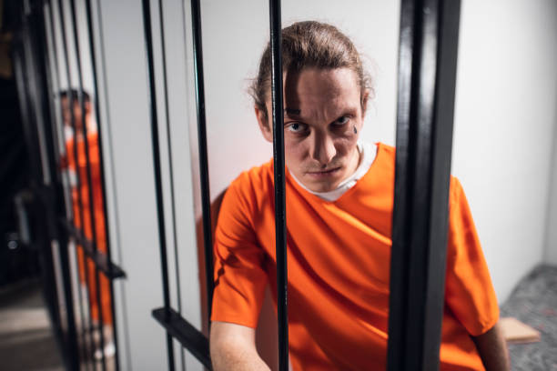 Psychological portrait of an evil and wild prisoner through the bars of a prison cell. A strong look and emotions stock photo