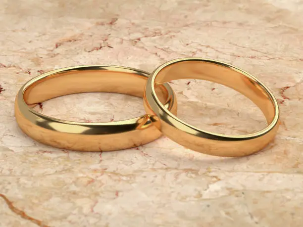 Two wedding gold rings lie next to each other on marble background. 3d rendering