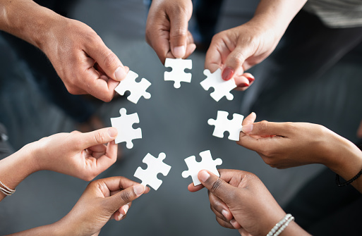 Close-up of many people hands holding a jigsaw puzzle piece in circle together.