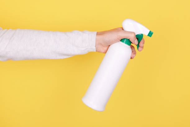 istock Hand with antiseptic in white spray bottle on yellow background. 1287567896