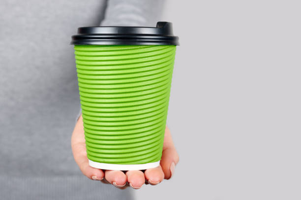 istock Hand with green disposal cup isolated on grey background. 1287568006