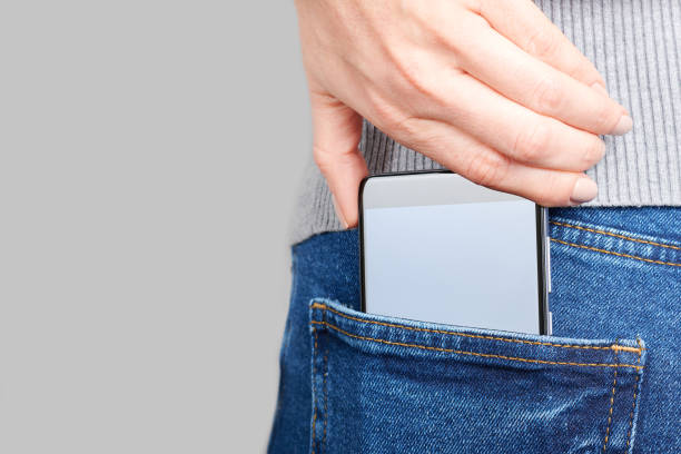 istock Hand with mobile phone in jeans pocket on grey background. 1287568427