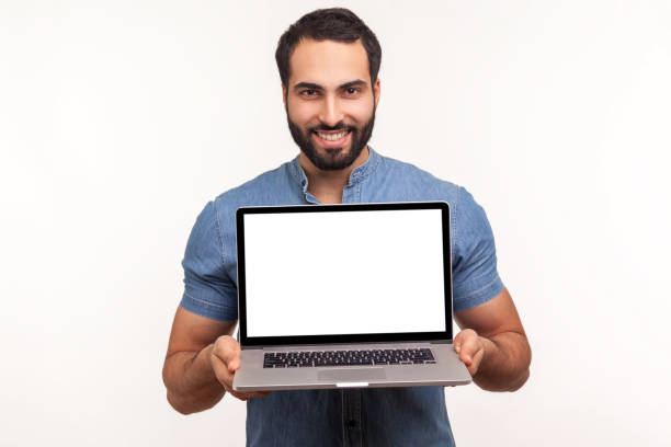 istock Successful bearded man in blue shirt holding and showing laptop with blank empty display, place for your advertisement, looking at camera with toothy smile 1287568464