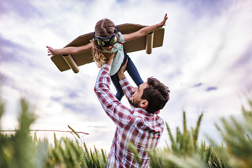 Happy little girl is pretending to be an airplane, while her father is holding her up in the air.