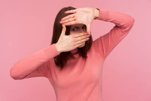 istock Serious female paparazzi with brown hair looking at camera through hands frame imaging camera, looking for suitable angle, spying 1287569387