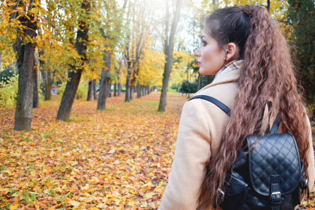 istock Woman standing in park with a back pack, autumn sanny day 1287569638