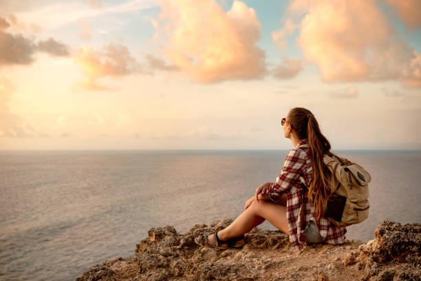 istock Girl with backpack sits on the cliff against sea 1287570167