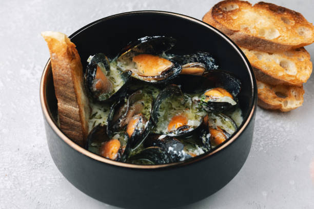 Cooked mussels with cream and white wine sauce, roasted toasts. Mediterranean cuisine. Concept for a tasty and healthy meal. Close up. Selective focus stock photo