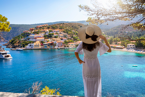 A tourist woman with white hat enjoys the view to the idyllic village of Assos on the island of Kefalonia, Greece, during summer vacation time