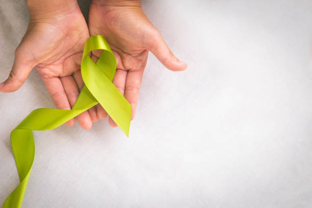 istock Hands holding light lime green ribbon on white fabric background with copy space. World Mental Health Day and Lymphoma Awareness symbol. Healthcare medical and insurance concept. 1287571409