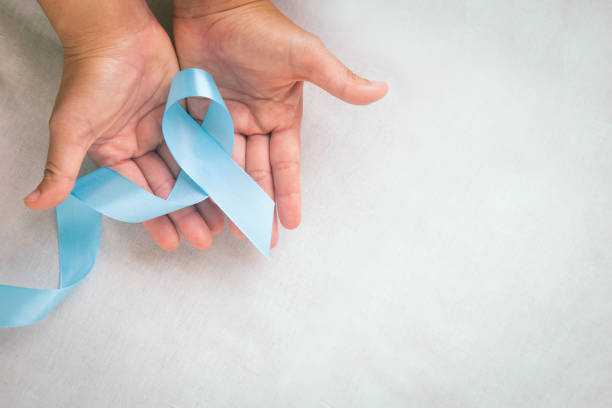 istock Hands holding light blue color ribbon on white fabric background with copy space. Lymphedema and Prostate Cancer Awareness month symbol. Healthcare medical and insurance concept. Male cancer. 1287571419