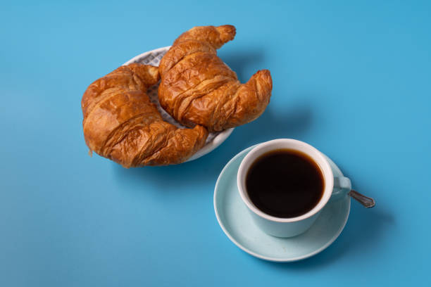 istock Cup of black coffee on blue background, with croissant, copy space for text. 1287571483