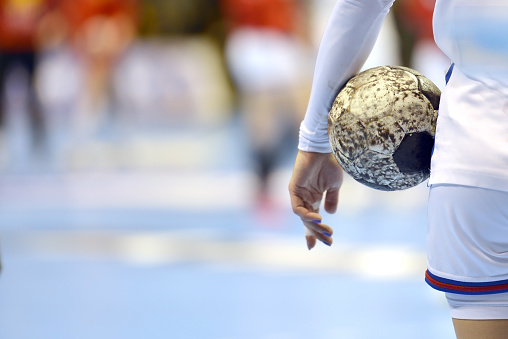 Closeup of a female handballplayer holding a handball, with copy space to the left side for text.