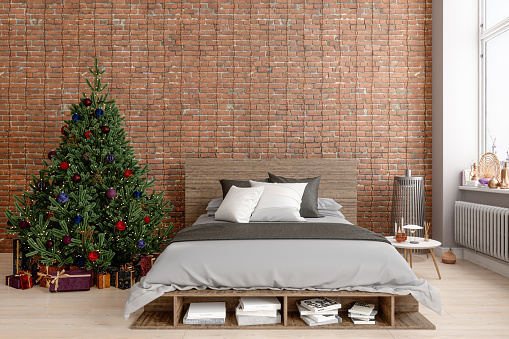 Christmas Tree With Ornaments And Wooden Bed Furniture With Gray Color Bedding In The Bedroom With Brick Wall Background.