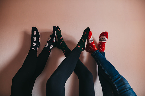 Close up legs of three young female friends in Christmas socks leaning on wall