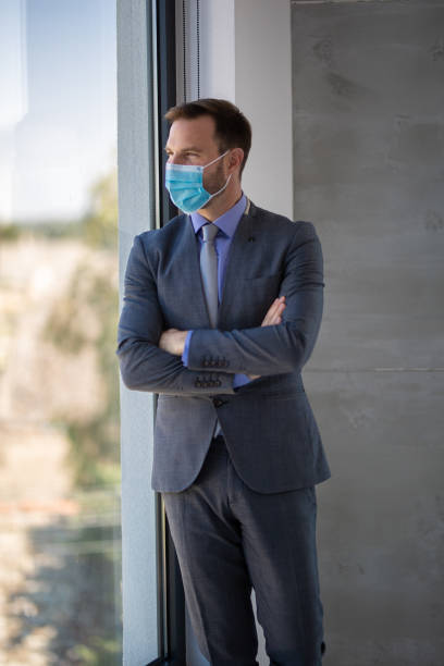 istock Businessman standing in modern office wearing protective facial mask 1287581349
