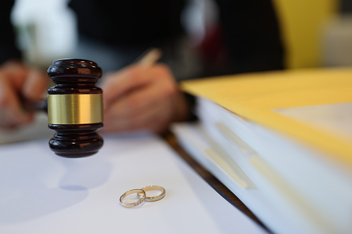 Judge holding wooden gavel near two wedding rings close-up. Pre-trial settlement of conflicts divorce concept