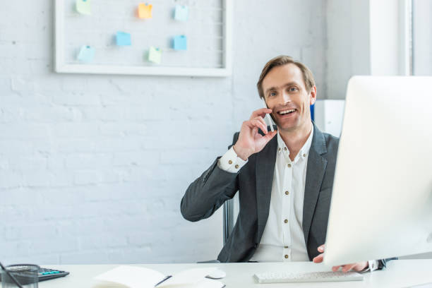 istock Smiling businessman looking at camera, while talking on phone, sitting at workplace 1287581574