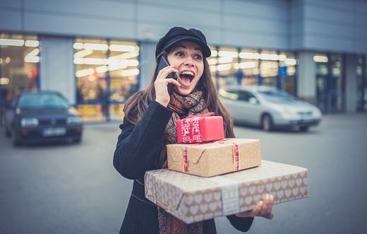 Portrait of beautiful woman holding Christmas presents and talking on the phone.