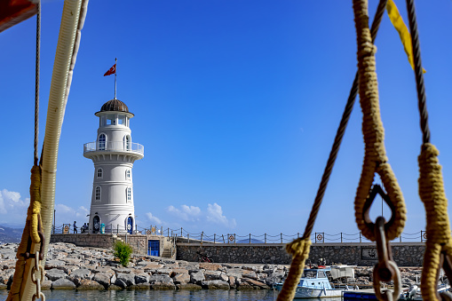 View from the deck of the ship to the Alanya Lighthouse through cables and ropes. Beautiful seascape with navigation equipment against the background of blue sky and water