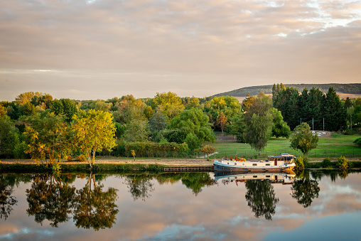 Boat on the Yonne river with reflections at sunset near Joigny in Burgundy, France.