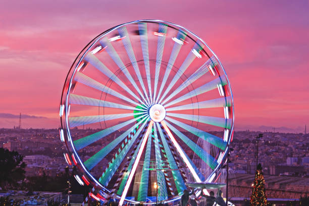 Rotating Ferris wheel against sunset pink sky and Malta cityscape. Christmas market in Valletta Square in December 2019. Aerial view, motion blur, selective focus