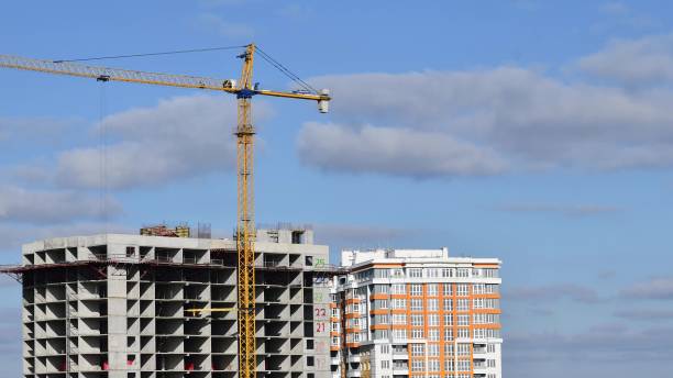 istock Construction crane jib and unfinished multistory building with clouds in sky 1287590976