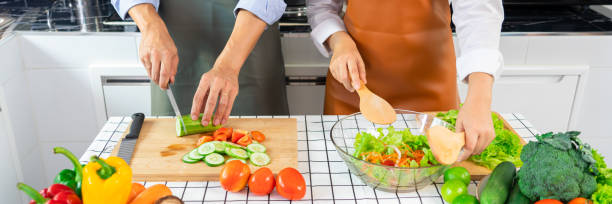 istock Happy couple having fun standing in kitchen at home preparing vegetable salad husband and wife vegetarians chop vegetables prepare for dinner in loft kitchen at home 1287592024
