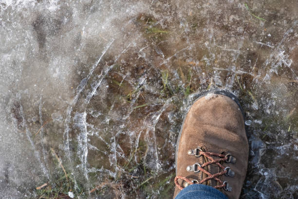 istock Man in brown nubuck boots is breaking or crushing ice. Waterproof boots. 1287592286