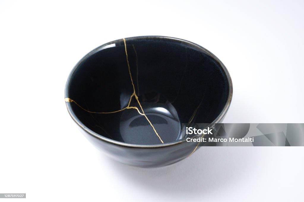 Kintsugi black bowl repaired with gold. Kintsugi black bowl. Gold cracks restoration on old Japanese pottery restored with the antique Kintsugi restoration technique. The beauty of imperfections. japanese pottery repair gold. japanese art of repairing cracks with gold. japanese art of fixing broken pottery Kintsugi Stock Photo