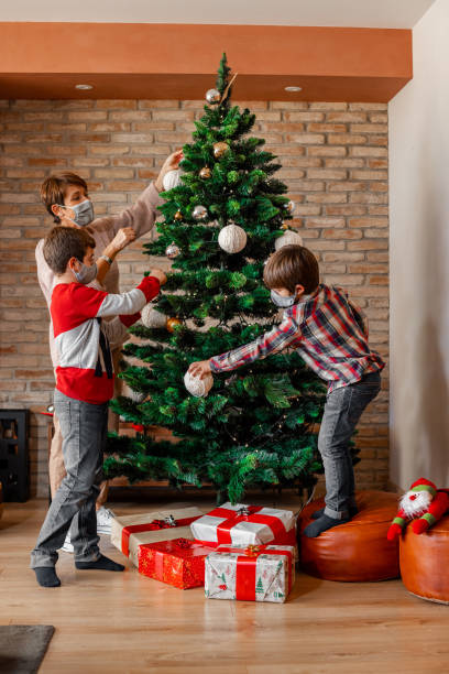 istock Family with face masks decorating christmas tree at home. 1287597114