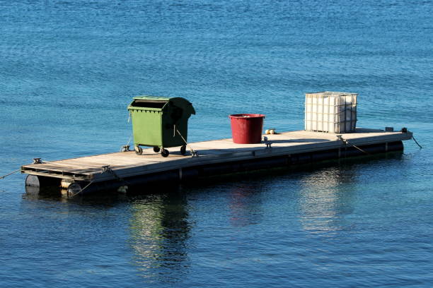 istock Large green plastic trash container next to big plastic barrel and white IBC plastic tank on top of elongated floating pier 1287598033