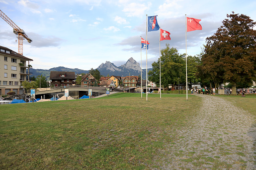 Brunnen, Switzerland - August 26, 2020: Large lawn behind which there are houses and mountain Mythen in the distance. There are four masts and there are four flags. This destination is one of the many great tourist attractions in Switzerland.