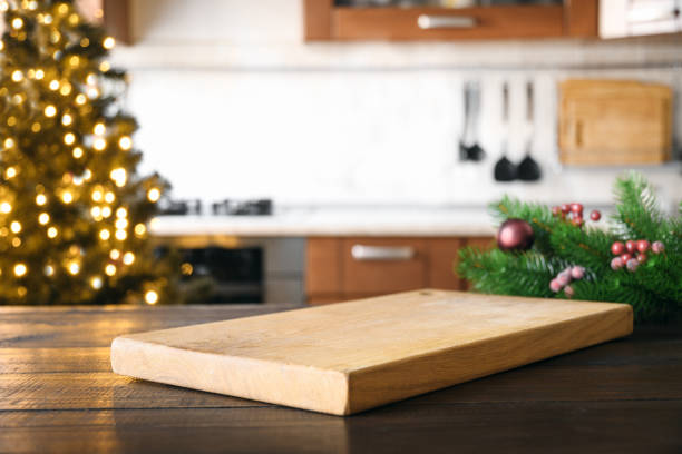 istock Empty cutting board on wooden tabletop with and blurred holiday kitchen decorated Christmas tree. 1287598755