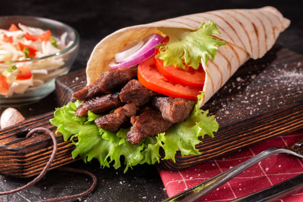 istock Handmade wrap shawarma is lying on the wooden cutting board. 1287601140