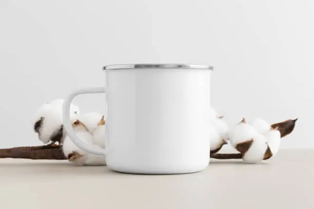 Enamel mug mockup with a cotton branch on a beige table.
