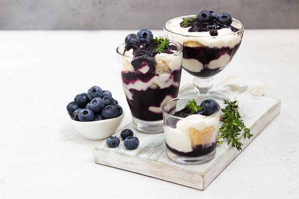 Tiramisu. Homemade dessert in glasses with blueberries, cream and ladyfingers garnish with blueberries and thyme. Light grey background. Tiramisu. Homemade dessert in glasses with blueberries, cream and ladyfingers garnish with blueberries and thyme. Light grey stone background. yogurt fruit biscotti berry fruit stock pictures, royalty-free photos & images